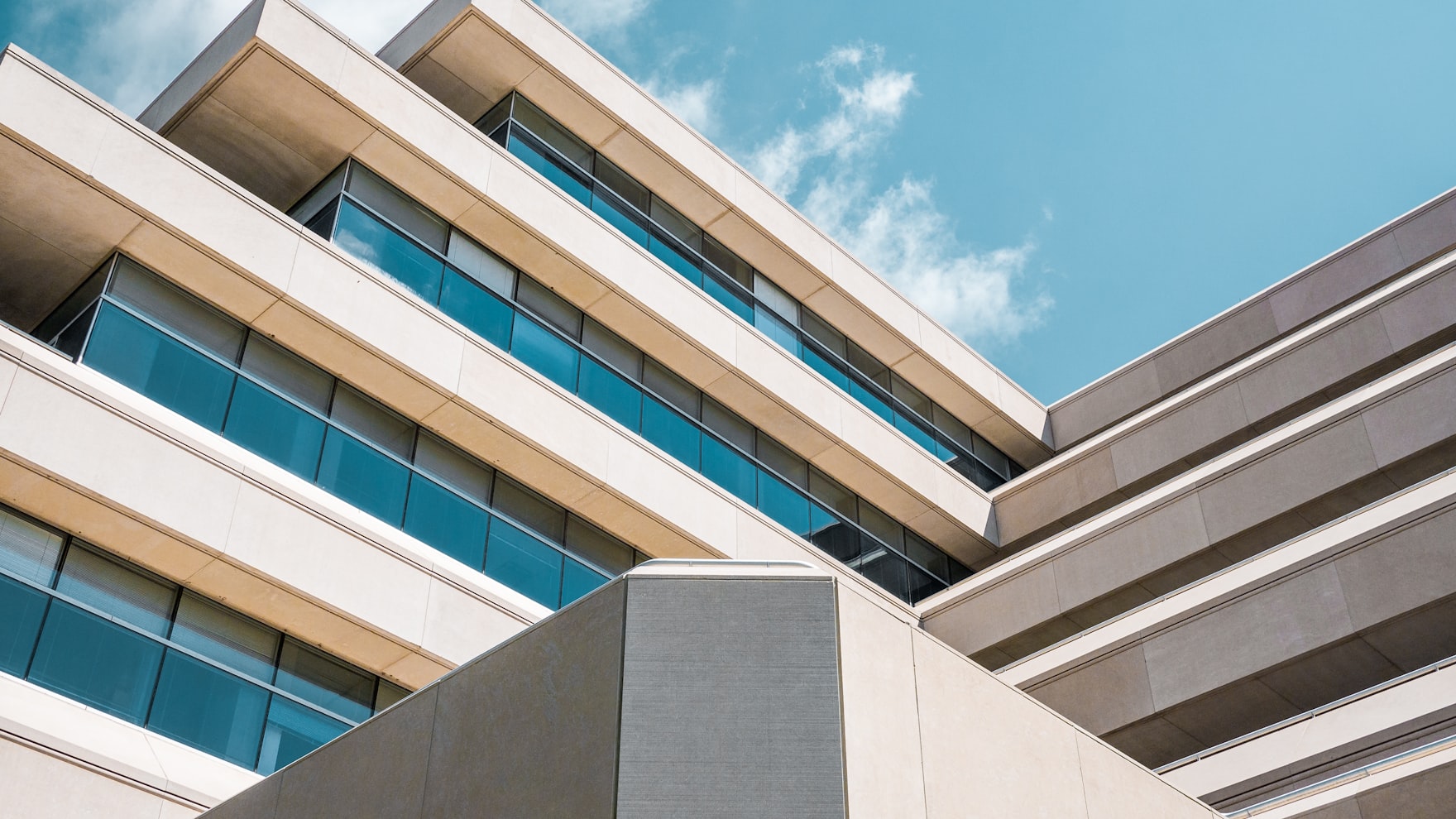 La façade vitrée et rythmée d’un bâtiment institutionnel moderne, vue en contre-plongée.